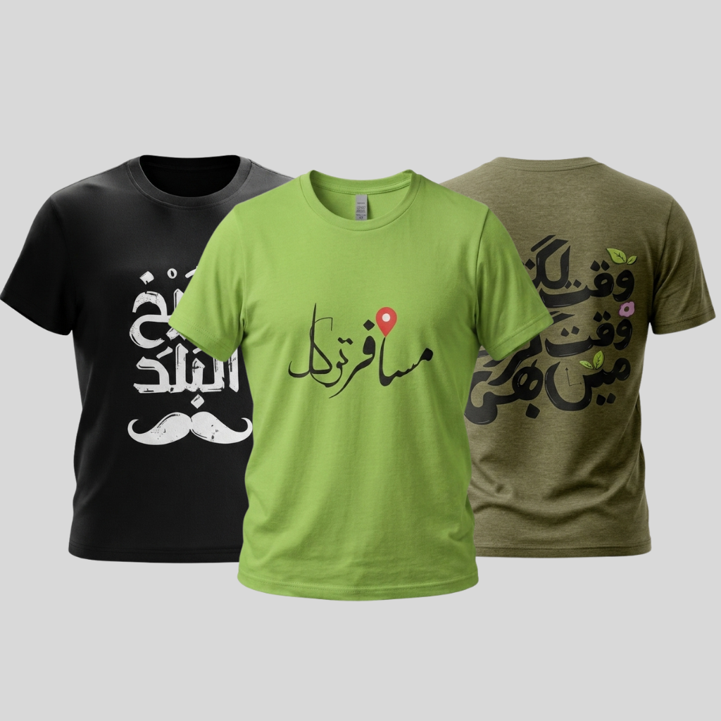 Three short-sleeve crew-neck t-shirts shown against a light gray background: a black shirt on the left with white Arabic calligraphy, a heather gray shirt in the center with peach Arabic text across the chest, and an olive green shirt on the right with white Arabic text and a white mustache graphic.