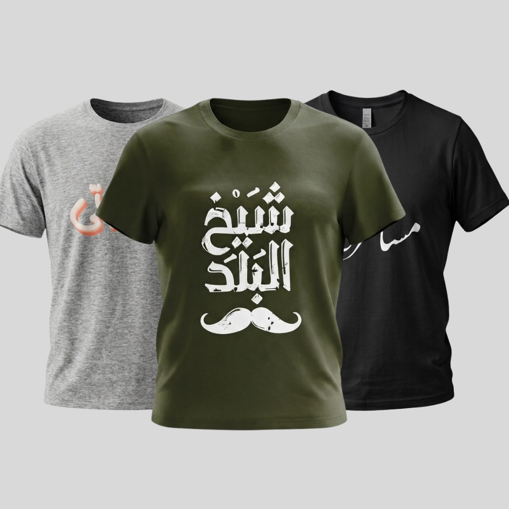 Three short-sleeve graphic T-shirts shown on a light gray background: a heather gray shirt on the left with a peach Arabic calligraphy print, an olive green shirt in the center with large white Arabic calligraphy and a white mustache graphic, and a black shirt on the right with a white Arabic calligraphy print.